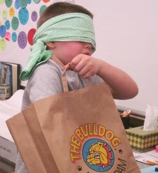 Student wearing a cloth blindfold and reaching into a paper bag
