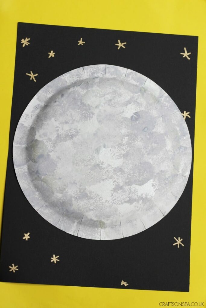 A black background has stars and a large moon made from a paper plate.