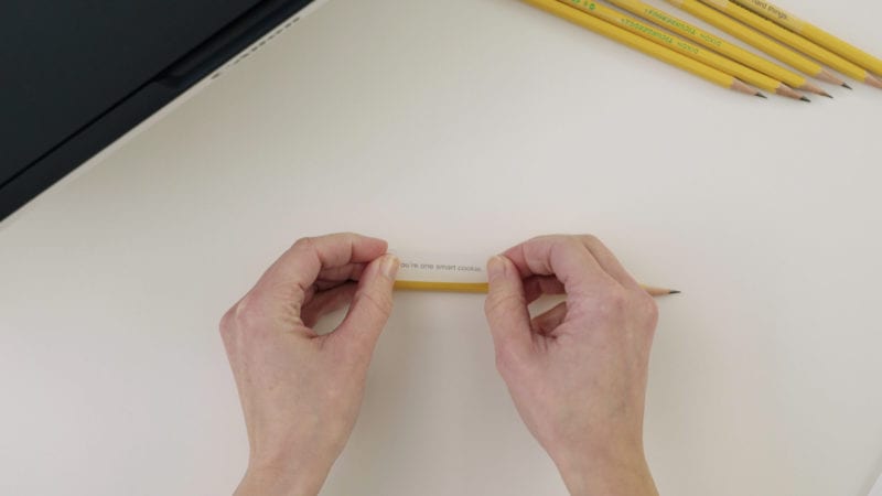 Hands putting tape with printed message on a pencil.
