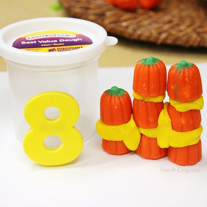 a yellow foam number 8 and 8 candy pumpkins stacked onto of each other with yellow playdough