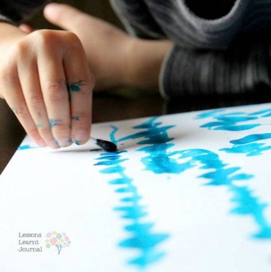 A child using a q-tip dipped in paint to draw a squiggly blue line
