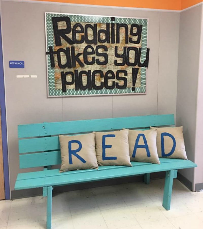 Reading Takes You Places bulletin board with a blue bench and pillows spelling out R E A D