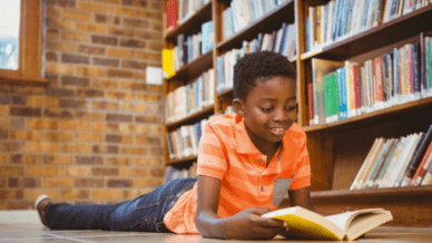 African American boy laying on ground in library reading a book - popular kids books