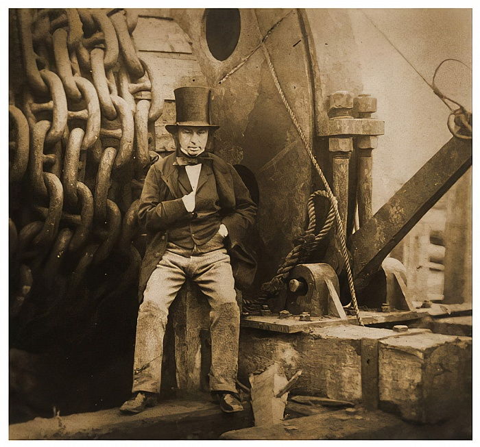 An old photo depicts a man standing in front of large machinery.