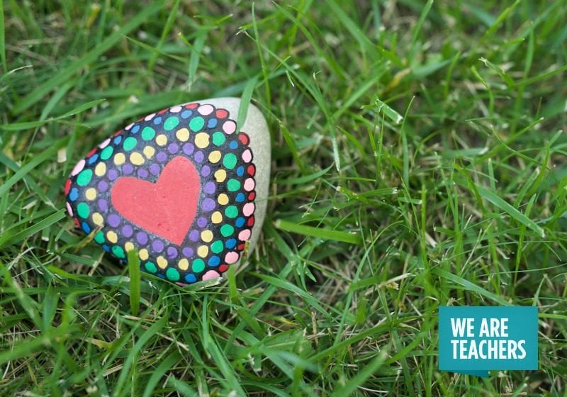 Heart painted on rock in the grass with the WeAreTeachers logo