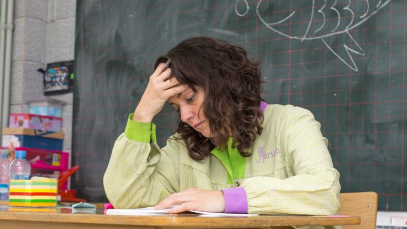 discouraged teacher sitting at her desk with her head in her hand