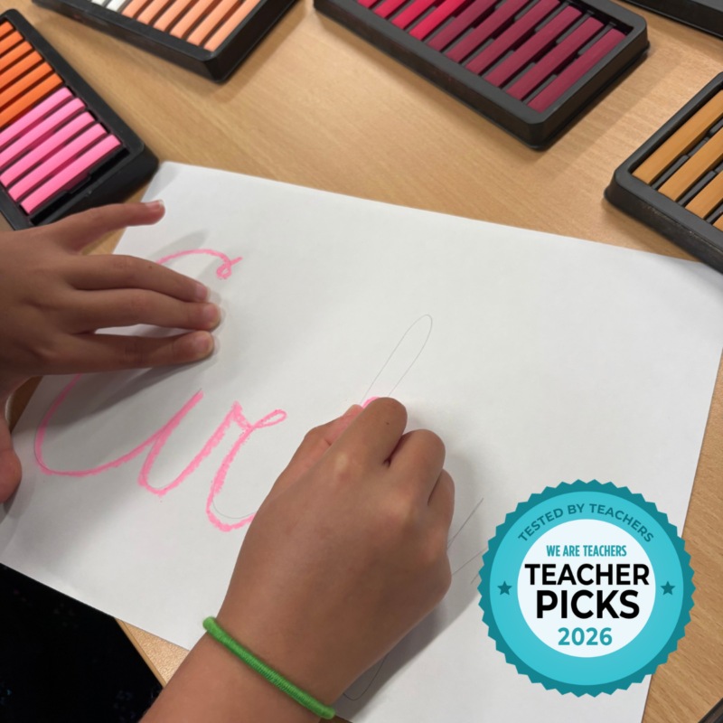 Student writing name on white paper in colored chalk.