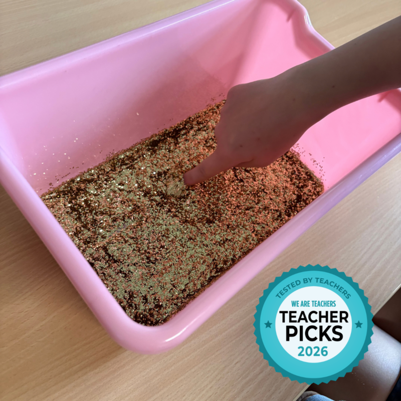 Student using finger to write name in a tub of glitter.