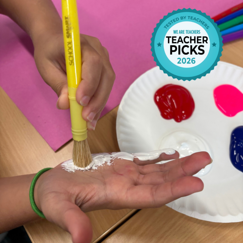 Student using a School Smart paint brush to apply white paint on the palm of their hand.