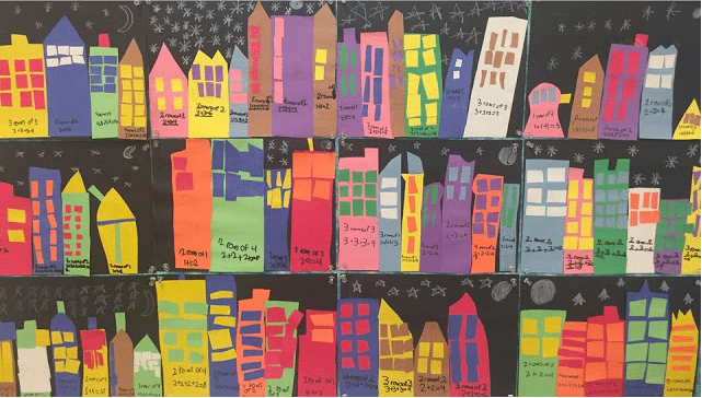 Cut-out building templates pasted on a wall with multiplication problems written on the buildings. 