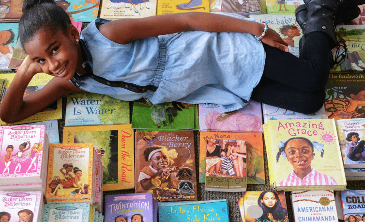 Marley Dias lying atop books with Black female characters