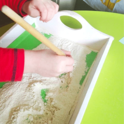 A child using a dowel to write in a tray filled with flour