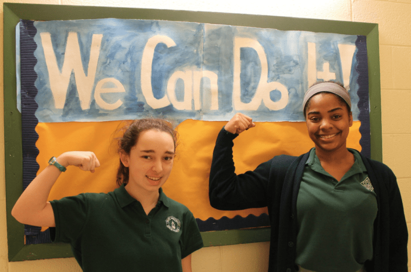 Girls flexing their muscles in front of poster that says We Can Do It!