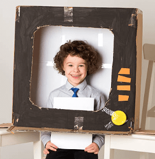 A cardboard box is made to look like a television set. The center has been cut out and a little boy stands in front of it making it appear he is "on tv." 
