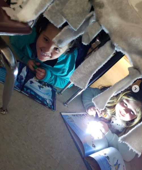 Two students nestled under their desks reading with flashlights as an example of read across america activities