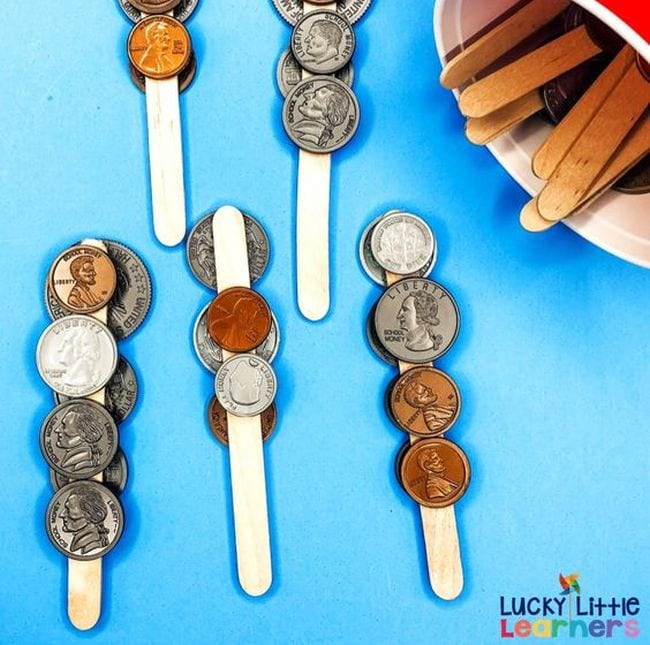 Wood craft sticks with plastic coins glued to them, used for second grade math games