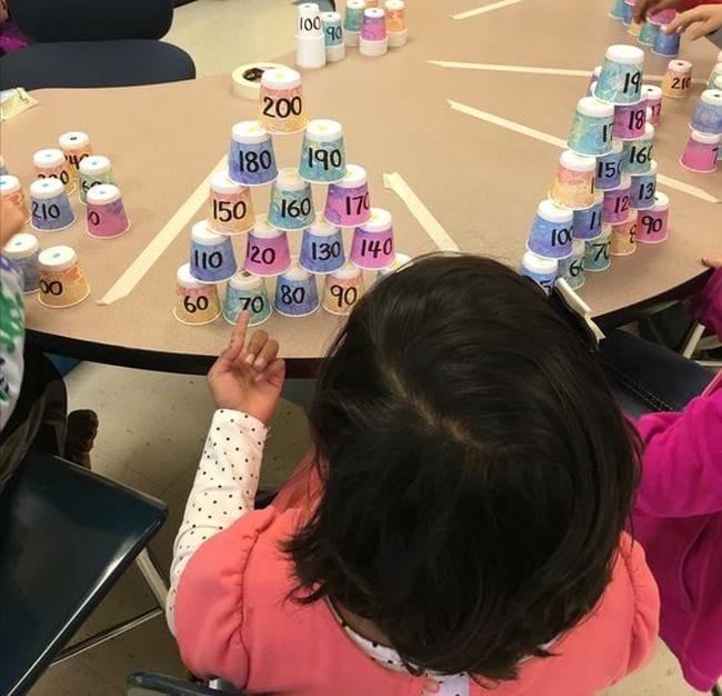 Second grade math students stacking paper cups labeled with numbers into pyramids