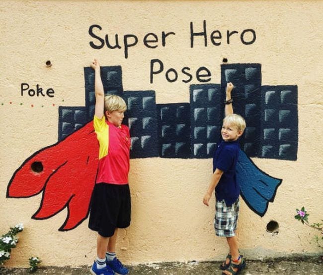 Two kids posing in front of capes and a cityscape painted on a wall