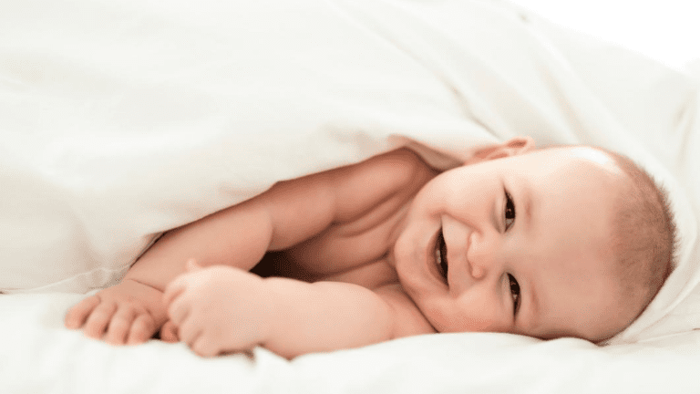 A baby smiling while wrapped in a white blanket.