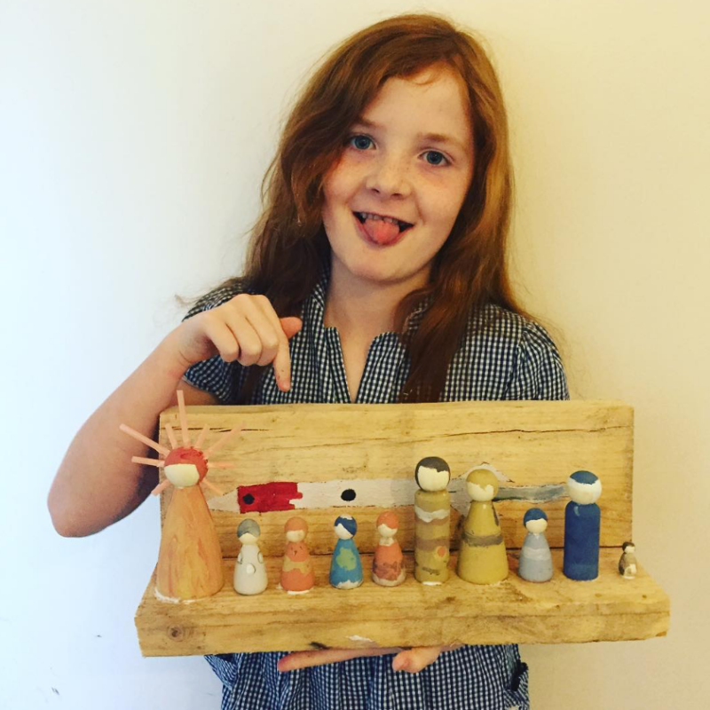 A little girl is holding a wooden box that has 9 peg dolls designed to look like the sun and planets.