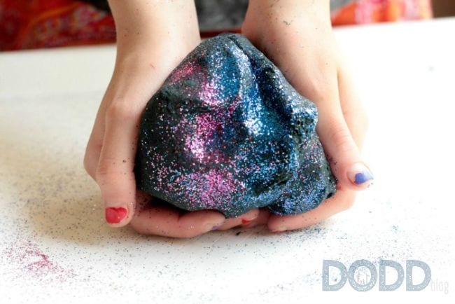 space activities for kids can be sensory like the one shown. Pictured here are two hands holding grey play dough flecked with pink and blue glitter