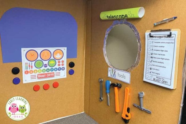 Space activities for kids can be play based like this play astronaut training center made from two sides of a cardboard box with colorful printouts attached, plus tools and a clipboard