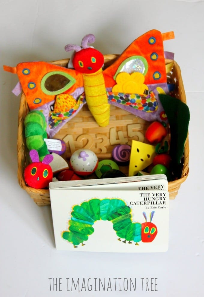 A basket filled with a plush caterpillar and items of toy food with the book The Very Hungry Caterpillar in front (Very Hungry Caterpillar activities)