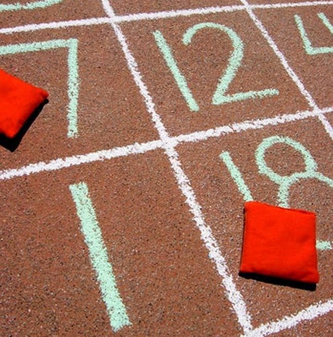 A grid of numbers written in chalk on the sidewalk with red bean bags in some squares 