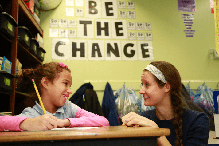 School counselor bending down to talk to student at desk.