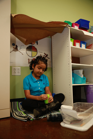First grade girl sitting on floor using a squeeze noodle.