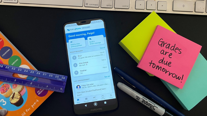 TalkingPoints app on cell phone screen which is on a teacher's desk with supplies.