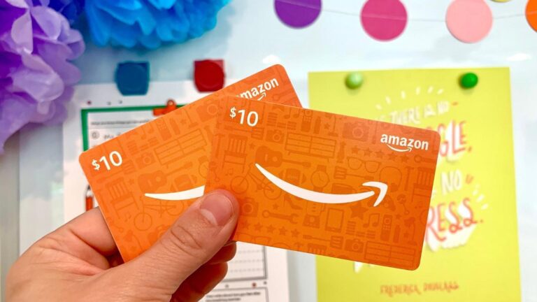Two amazon gift cards held up in front of a colorful whiteboard.