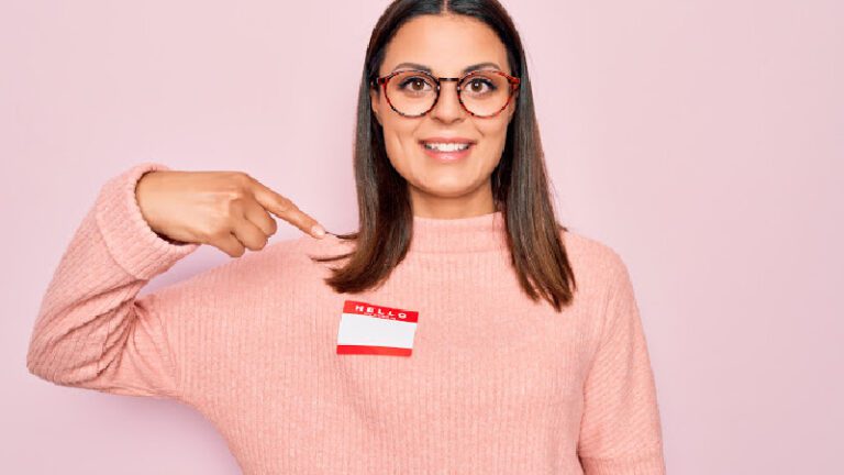 Young woman pointing to nametag on pink sweater 5 Alternative Teacher Names to Try in Your Classroom This Year