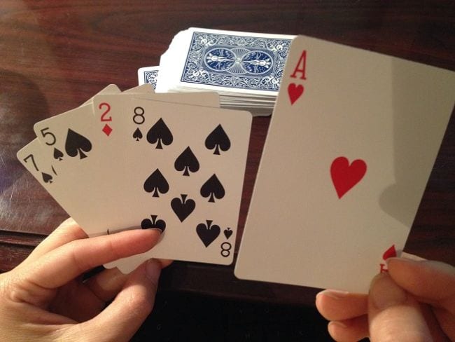 Hands holding playing cards in front of a stack of cards