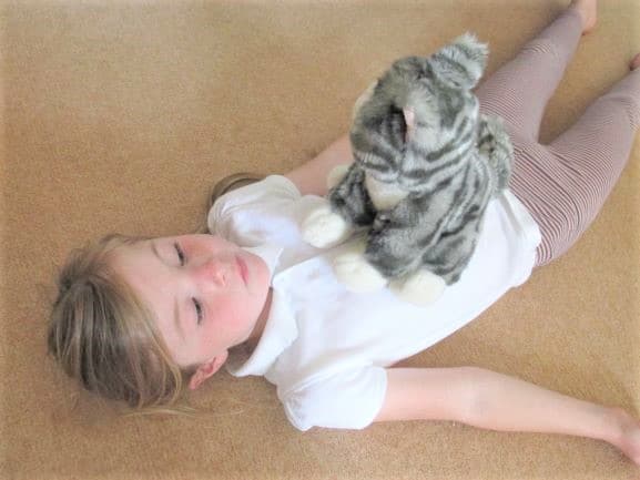 A young girl lies on the floor with a stuffed kitten on her chest