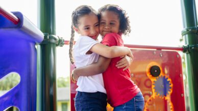 Elementary aged Hispanic best friends hugging on playground - The Compassion Project