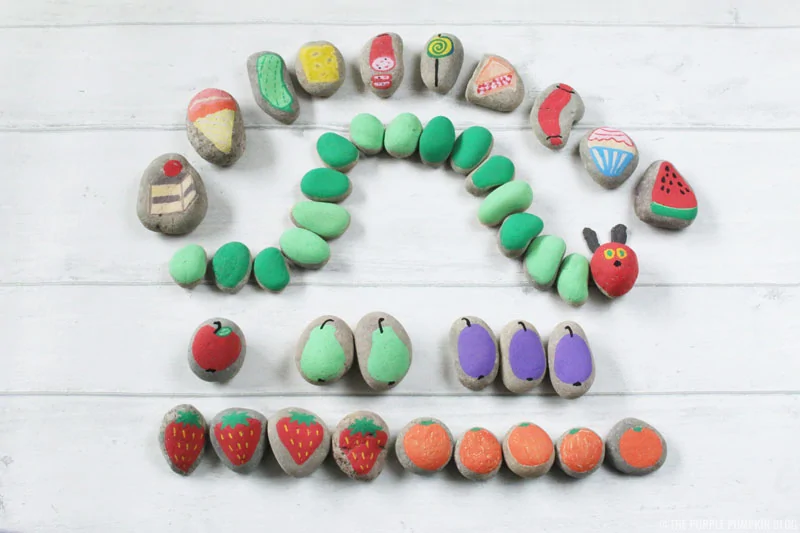 4 rows of rocks are painted with fruits and vegetables and one row is made to look like a caterpillar.