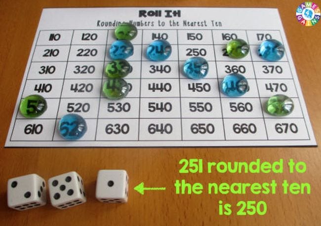Roll It rounding game with markers and dice showing 2, 5, and 1. Text reads 251 rounded to the nearest ten is 250.