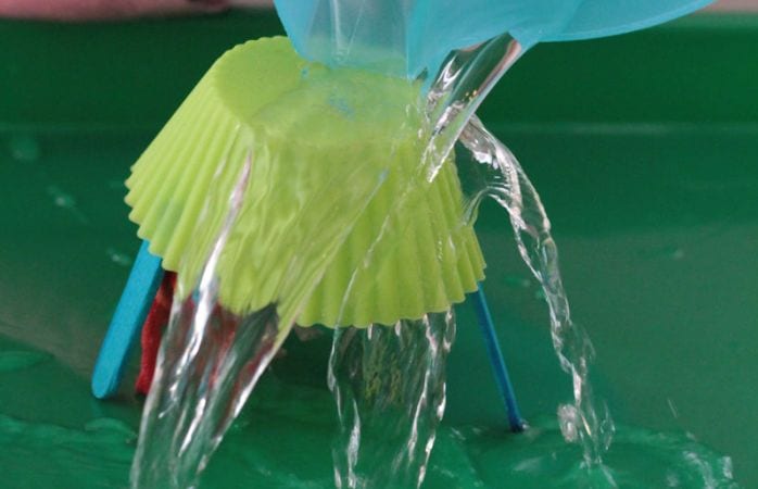 Science student pouring water over a cupcake wrapper propped on wood craft sticks