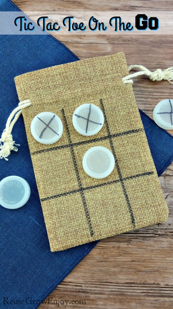 A burlap bag has a tic tac toe grid drawn on it in permanent marker. bottle caps either have X's drawn on them or are left blank on the tic tac toe board. 