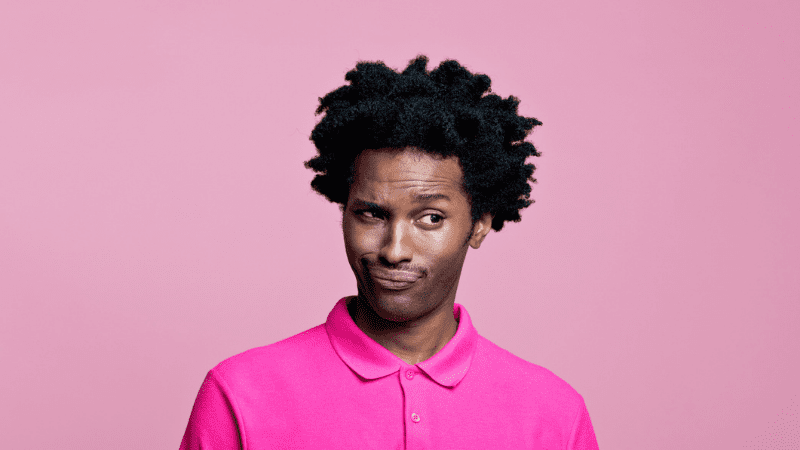 Black man in bright pink shirt with an incredulous expression on his face in front of a light pink background