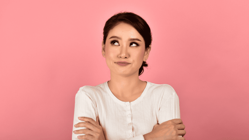 Woman in white shirt rolling her eyes in front of pink background