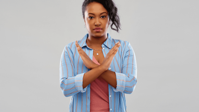 Black woman making a "no" gesture by crossing her arms in front of her chest 