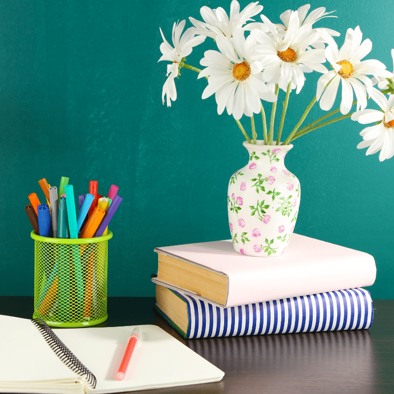 Flowers in a vase sitting on a desk with books and pens