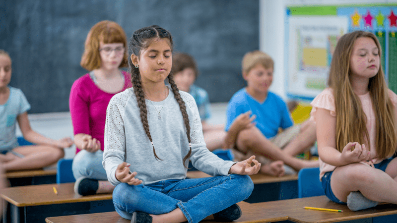 Photo of students sitting on their desks participating in a guided meditation