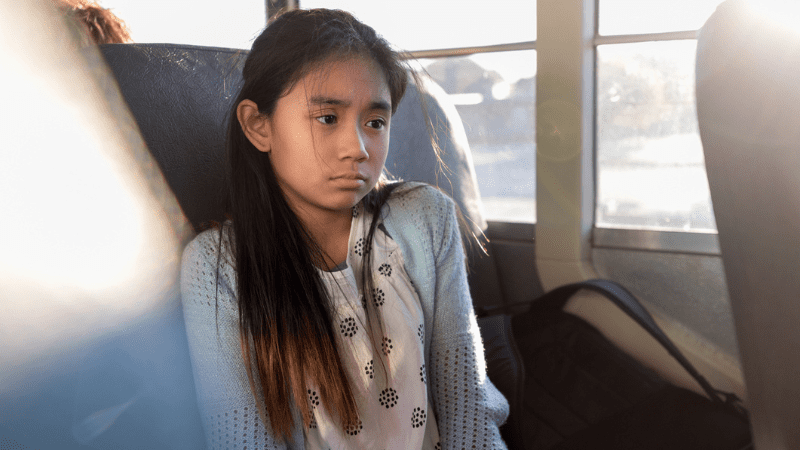 Sad Asian girl sitting alone in a school bus seat