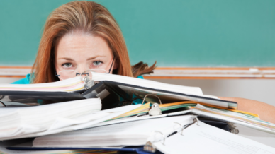 Exhausted teacher staring over a stack of binders and paperwork