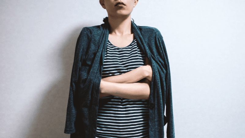 Young woman standing in front of white background in a tshirt and cardigan that is draped around her shoulders