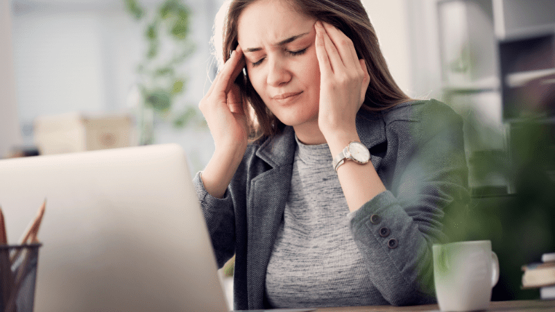 Brunette woman looking at a laptop while rubbing her temples, as an example of a symptom of poor school air quality