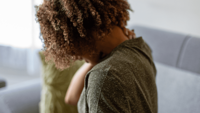 Black woman with her back facing us as she rubs her neck in discomfort